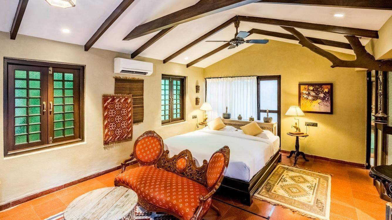 Elegant premium hut suite featuring a spacious bedroom with rustic wooden furnishings, plush bedding, and private outdoor seating area overlooking the lush garden at Ramsukh Resort